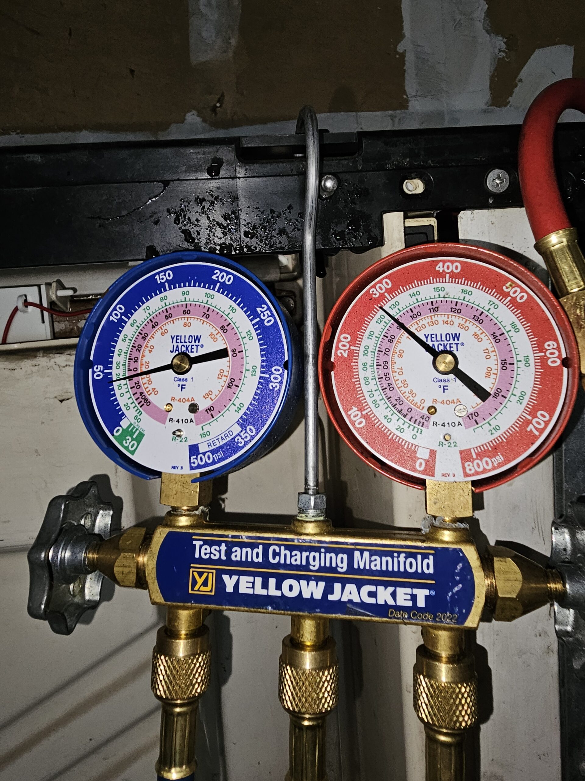 Technician using a manual refrigerant gas measuring tool to check a commercial refrigerator system in Seattle.