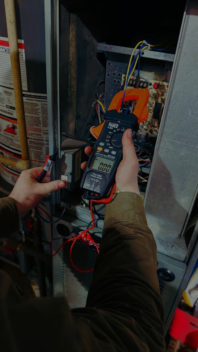 HVAC repairman using a digital multimeter to test the electrical control board of a residential heating system during a diagnostic visit.