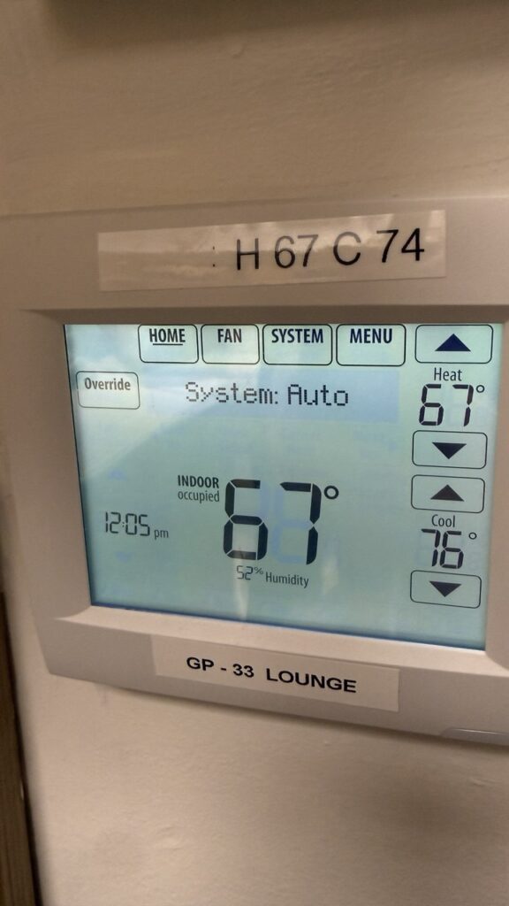 Commercial digital thermostat in a lounge area displaying a 67-degree indoor temperature and humidity levels monitored by A/C Dr. Naz.