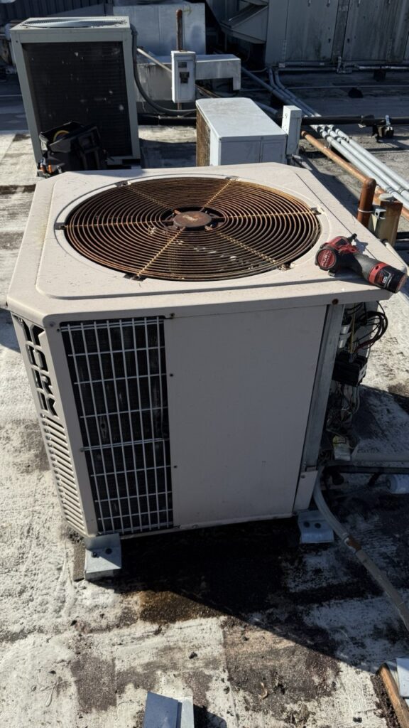 Technician performing electrical diagnostics on a York commercial air conditioner on a Seattle rooftop, showing exposed capacitors and wiring.