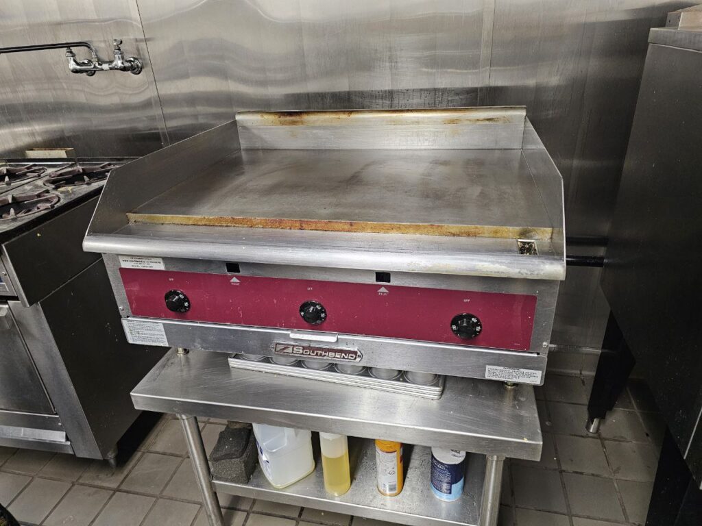 Professional countertop gas hot plate in a Seattle kitchen with misaligned burner caps and worn grate supports awaiting surface-level maintenance.