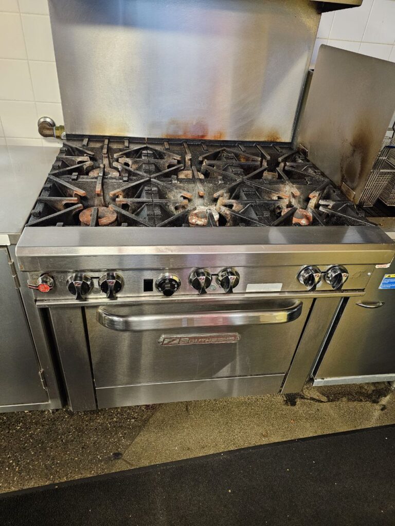 Close-up of a clogged commercial gas burner head on a Seattle cooktop showing carbon buildup and grease obstruction in the burner ports before restoration.