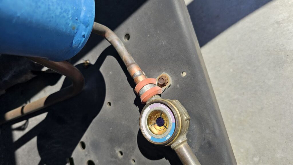 Close-up of a refrigerant liquid line sight glass. The indicator shows a dark purple/blue center, suggesting a dry system, surrounded by a "Caution" and "Dry" color-coded ring.
