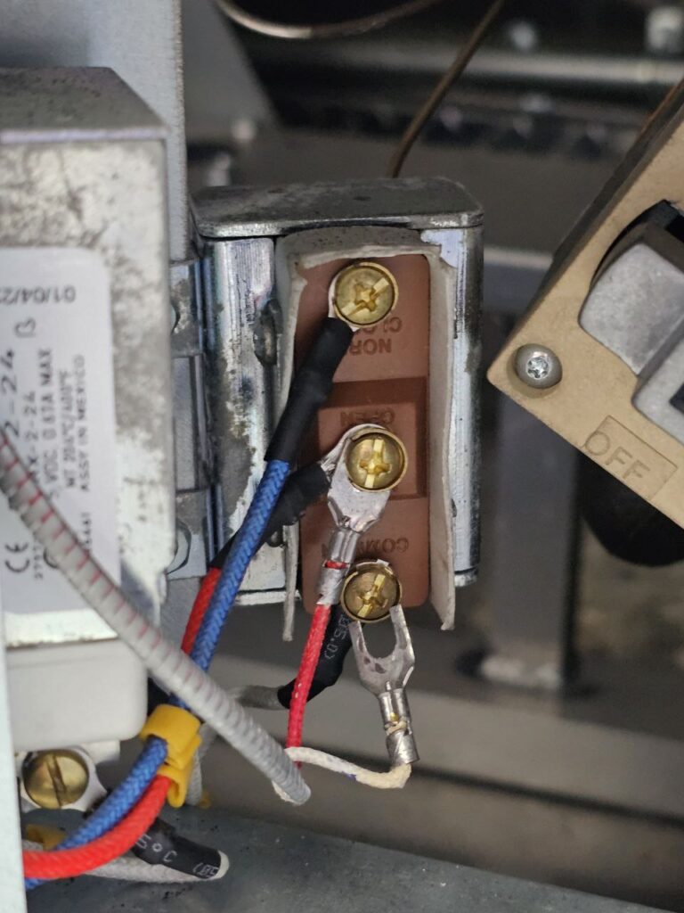 A macro shot of a commercial fryer's high-limit thermostat or electrical contactor block, showing terminal screws and wiring connections (blue, red, and white) responsible for temperature control and safety shut-off.