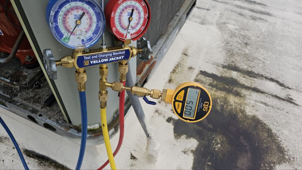 A professional HVAC technician's setup on a rooftop, showing a vacuum pump and refrigerant tank connected via yellow and blue hoses to a Trane rooftop unit during a repair.