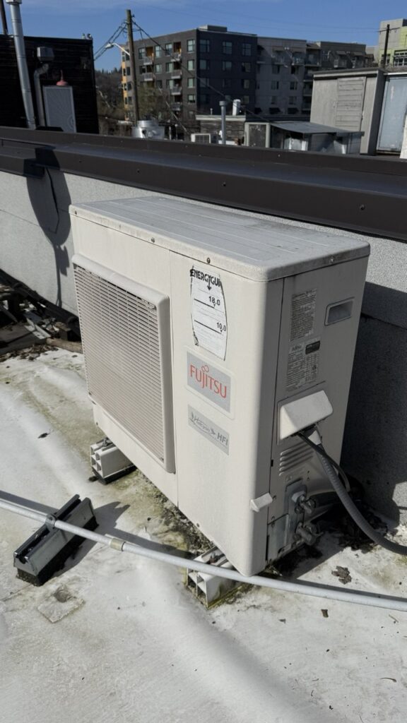 Fujitsu Halcyon commercial mini-split outdoor unit being serviced on a Seattle rooftop with urban buildings in the background.