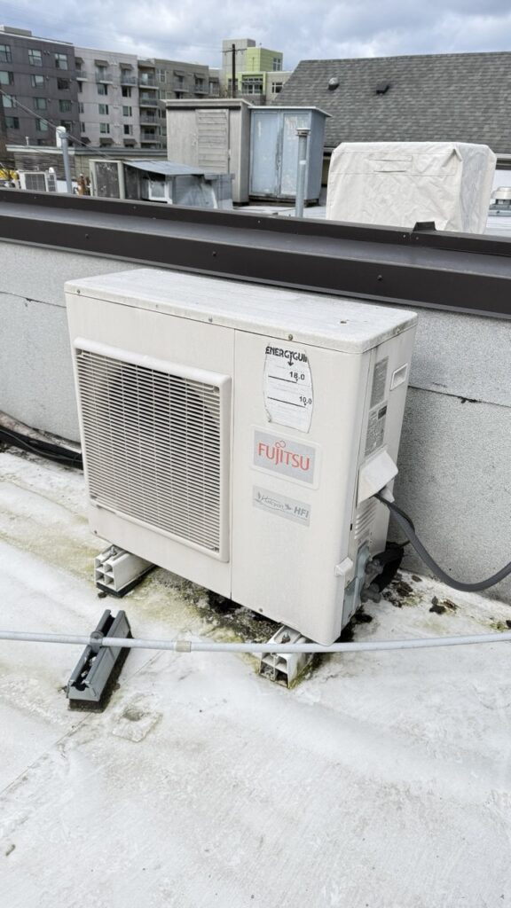 Professional repair and maintenance of a Fujitsu commercial heat pump system located on a multi-family building rooftop with the Seattle city skyline in the background.