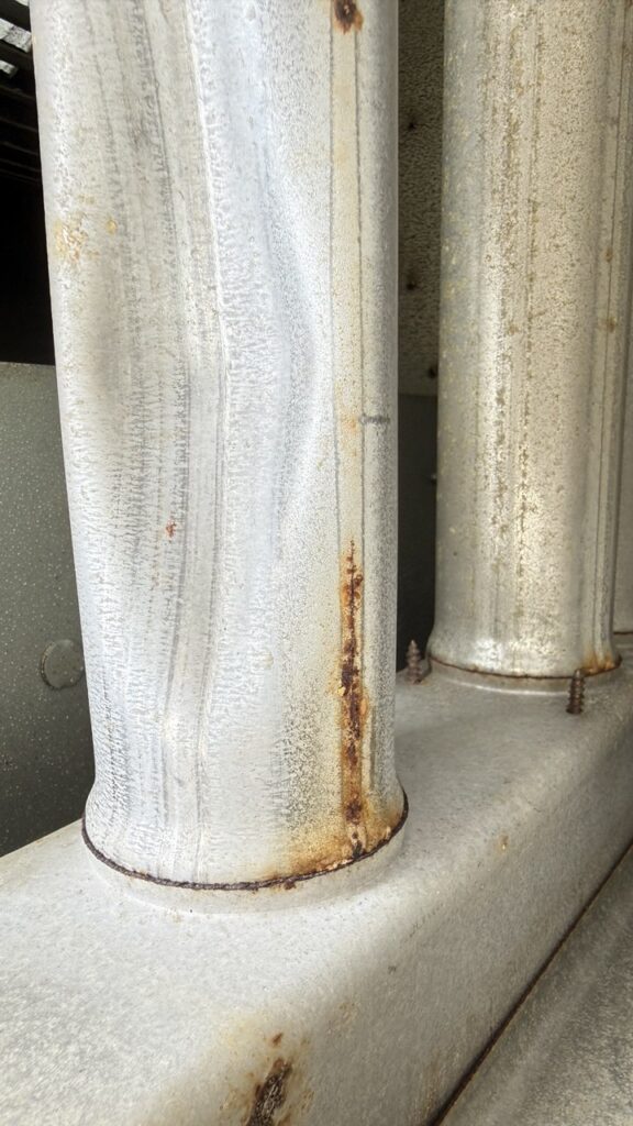 Close-up inspection of rusted heat exchanger tubes in a commercial rooftop unit during a Seattle maintenance call to prevent carbon monoxide leaks and ensure system safety.