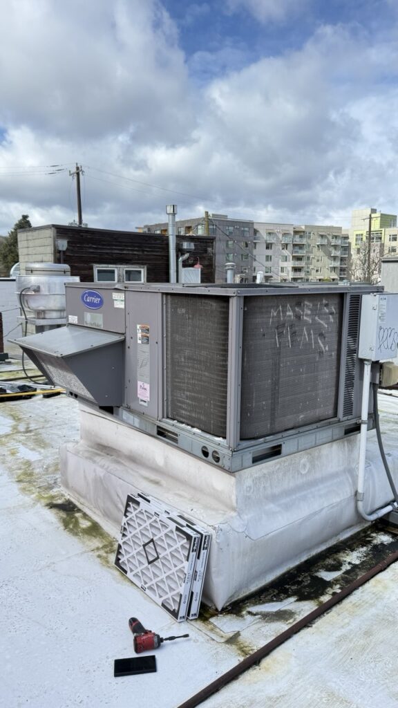 Exterior view of a Carrier WeatherMaker rooftop unit during a commercial HVAC maintenance service in a Seattle urban neighborhood.