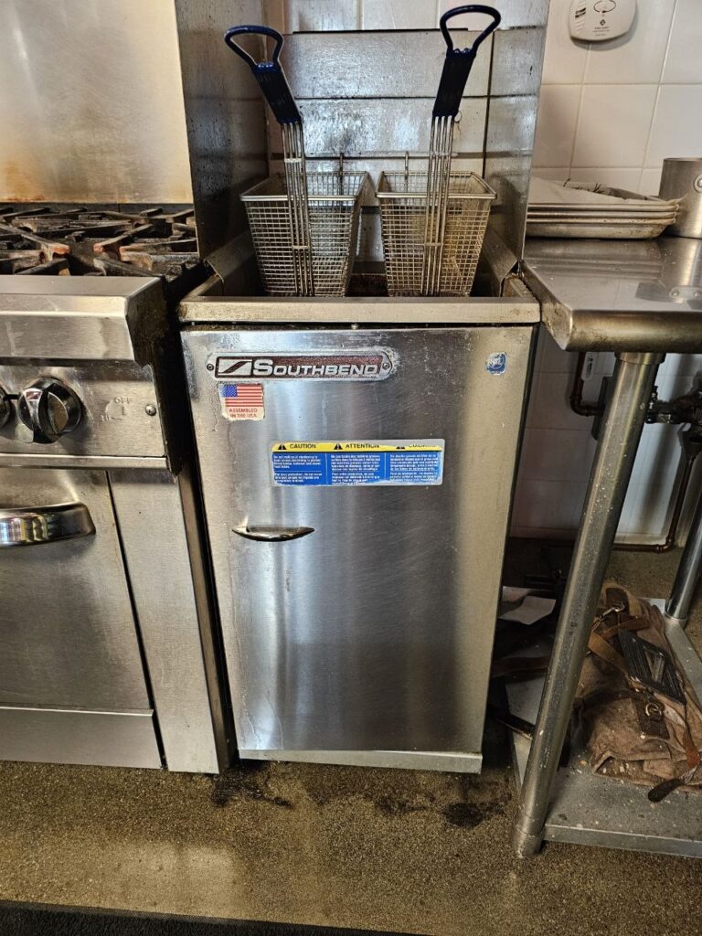 A Southbend commercial floor fryer situated in a cook line next to a range, featuring stainless steel construction and dual baskets, ready for a pilot light or thermostat inspection.