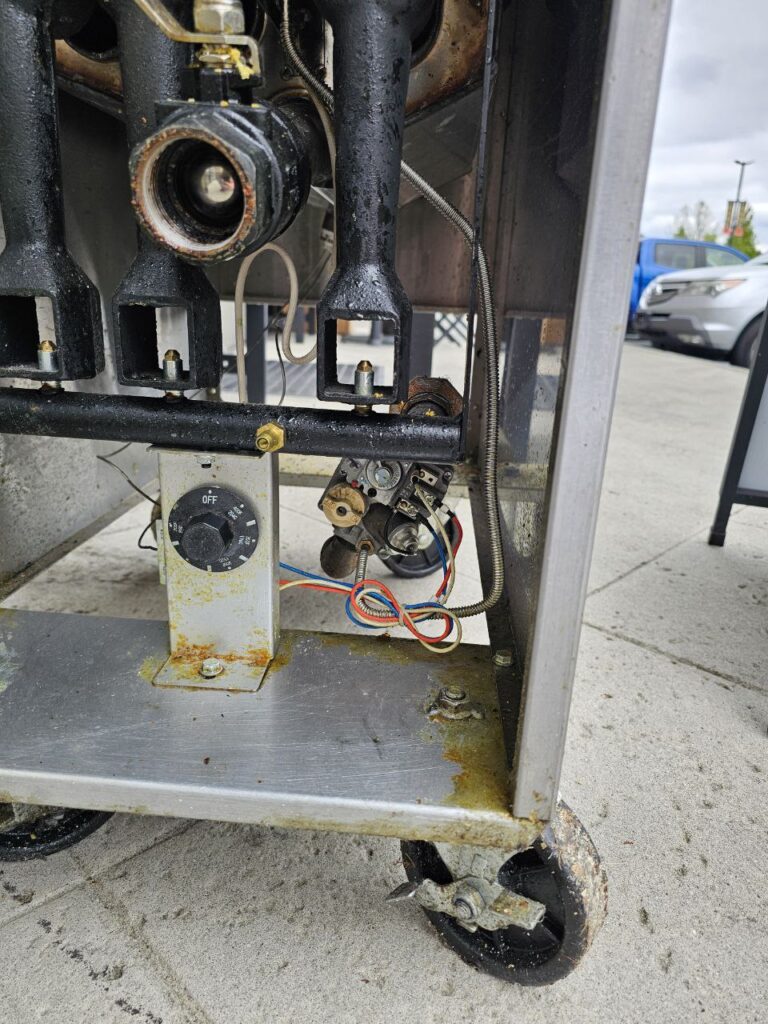 A modern Frymaster commercial fryer bank in a Seattle kitchen, featuring digital control interfaces and a front-access panel opened for a diagnostic inspection of the internal components.