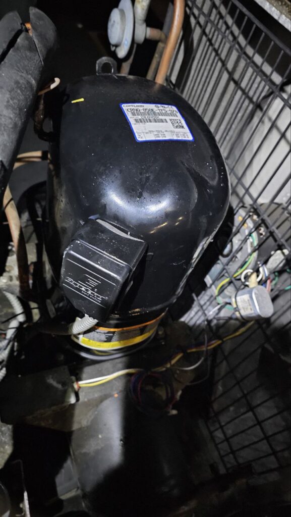 A black Copeland reciprocating compressor (Model CRNQ-050E-TF5-970) installed inside a commercial AC unit, showing the electrical terminal box and copper piping.