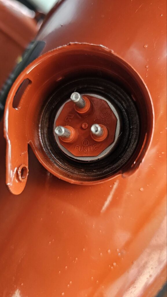 An overview of the open maintenance compartment of a Trane rooftop unit. The image shows the red compressor at the center, surrounded by complex electrical wiring, contactors, and control boards. A blue tool case and various hand tools are visible, indicating an active repair in progress.