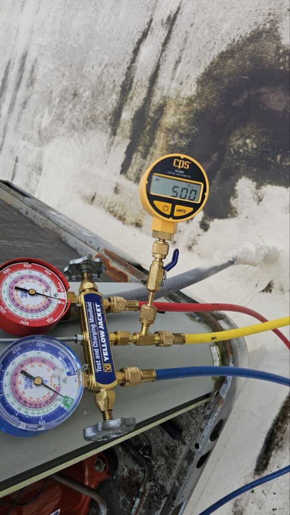 Precision refrigeration diagnostic testing on a commercial rooftop unit using professional-grade manifold gauges and a digital vacuum micron gauge.