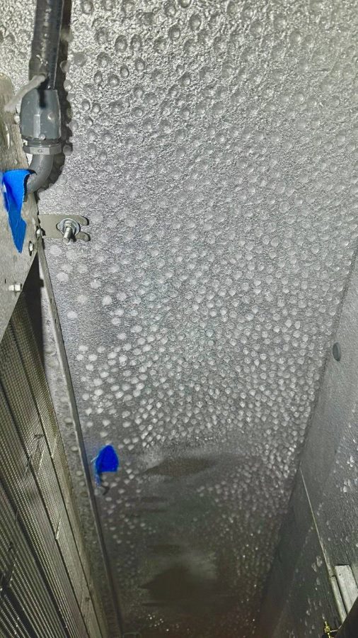 Close-up of walk-in freezer interior panel covered in frost and frozen condensation near evaporator fins, with insulated line and blue tape markers.