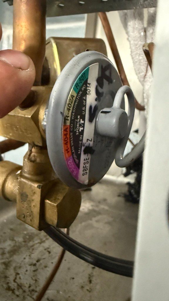 Technician hand on a Sporlan thermal expansion valve during walk-in cooler repair