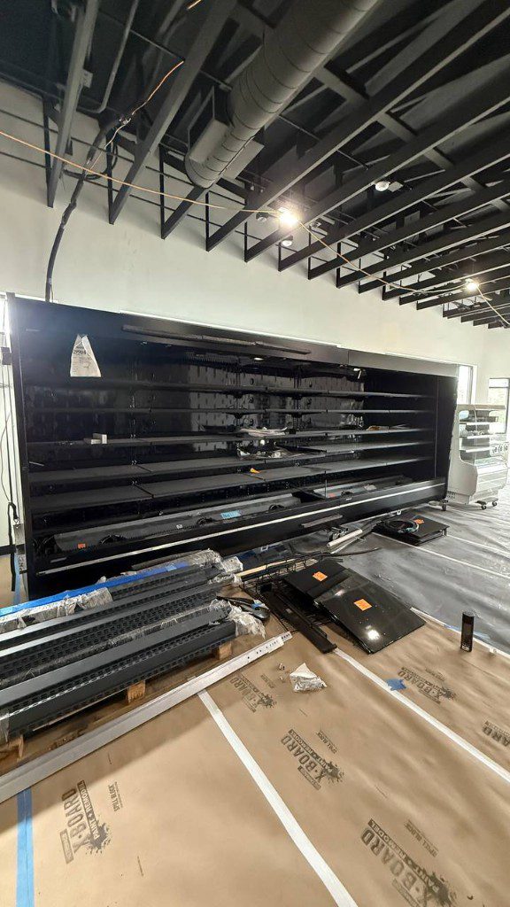 Field photo of black multi-deck refrigerated display case during store build-out — serves Newcastle, WA commercial refrigeration repair