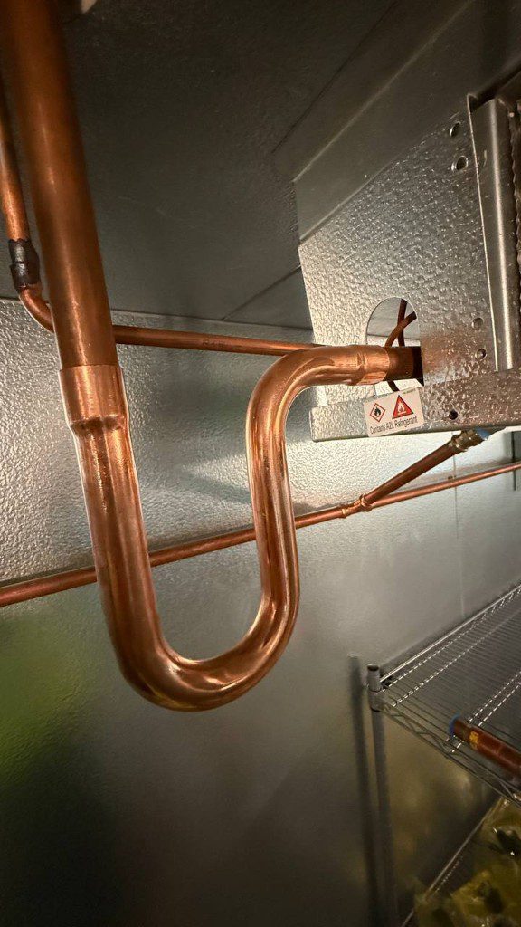 Field photo of copper U-trap piping into a commercial refrigeration enclosure — serves Sammamish, WA commercial refrigeration repair